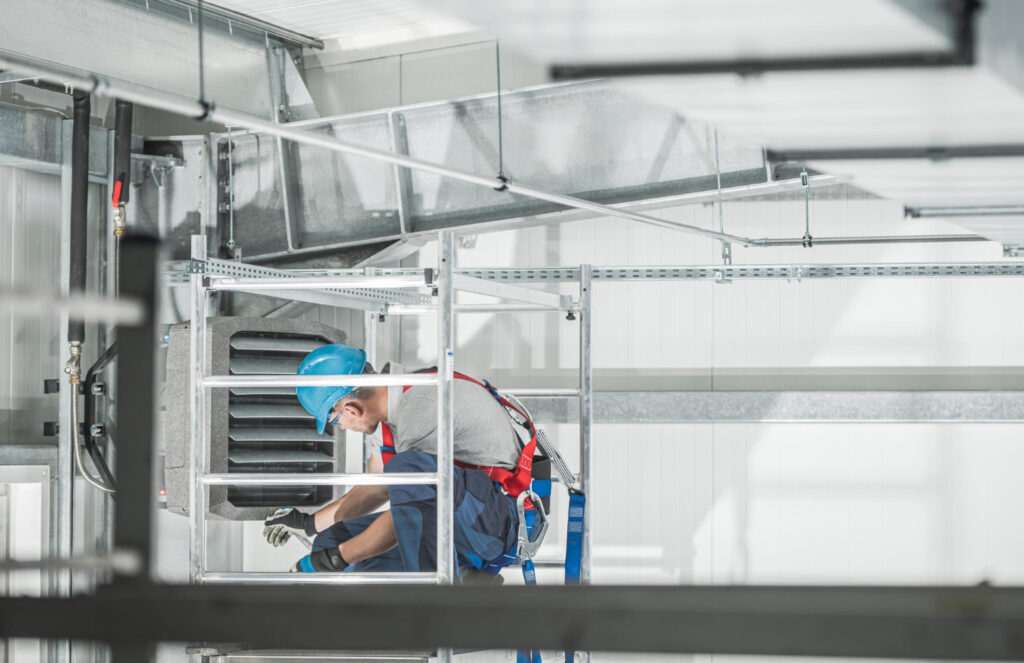 A man wearing a hard hat and safety vest is diligently working on a metal ladder at a construction site.