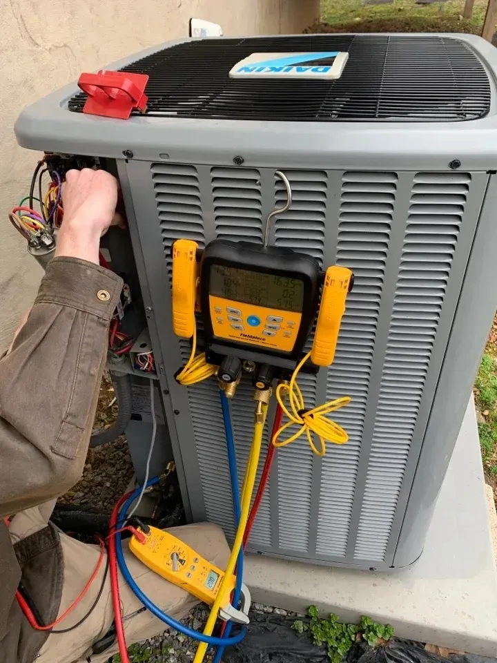 Technician servicing an outdoor air conditioning unit with diagnostic tools.